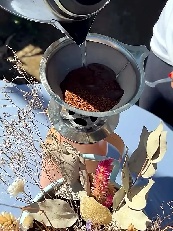 Café sendo coado no filtro de inox, com arranjo de flores secas