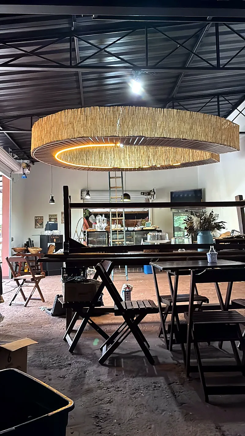 Salão do café com mesas de madeira e lustre de palha